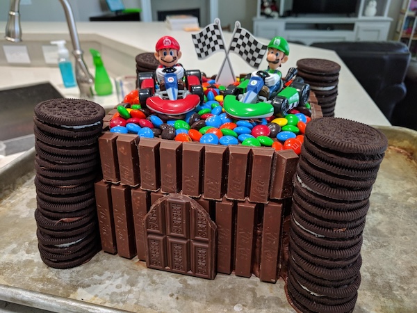 Cake surrounded by Oreos, Kit-Kats, and topped with M&Ms and Mario Kart toys